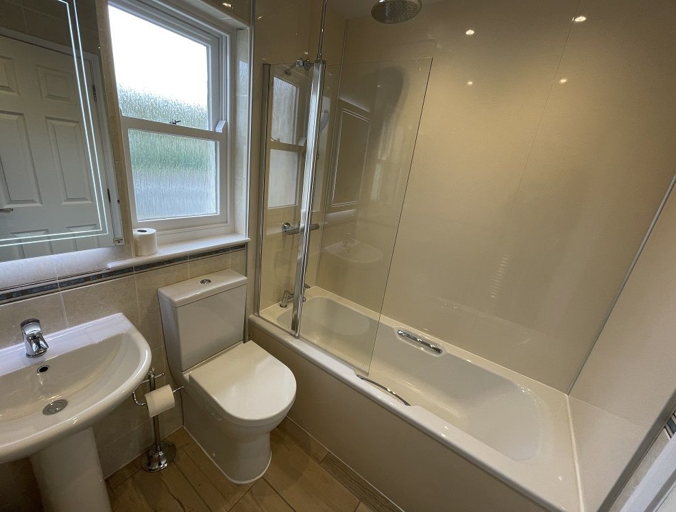 The modern bathroom features a bath with overhead shower, WC and hand sink