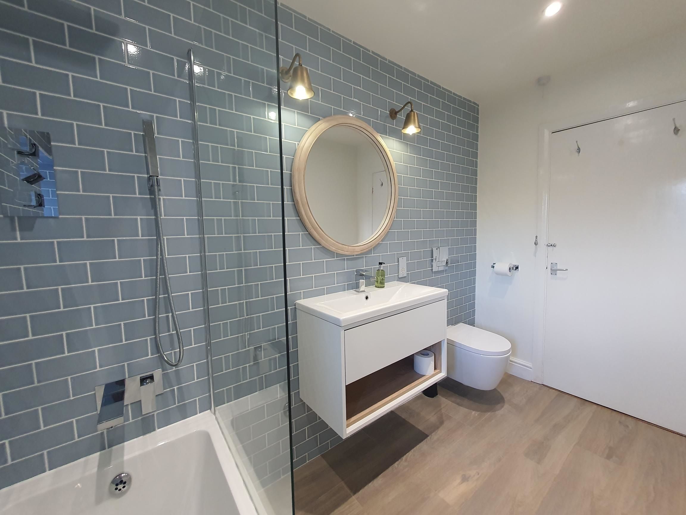 The bathroom has a bath with overhead shower, hand basin and WC