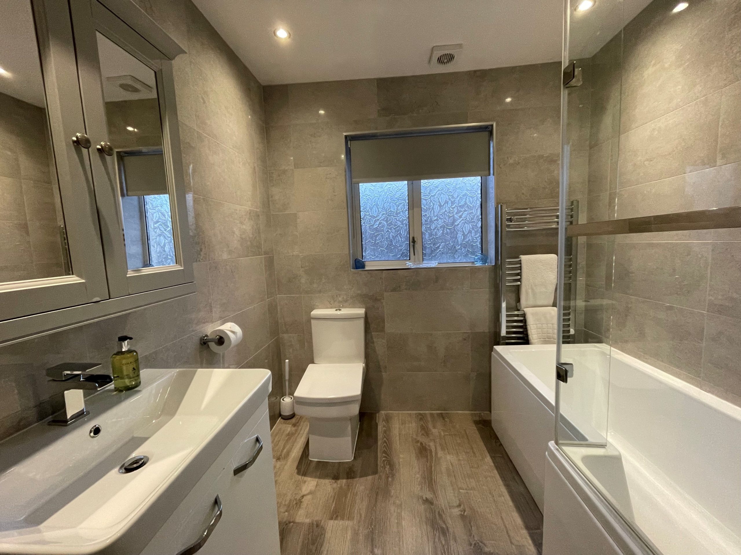A modern fitted bathroom with bath and overhead shower