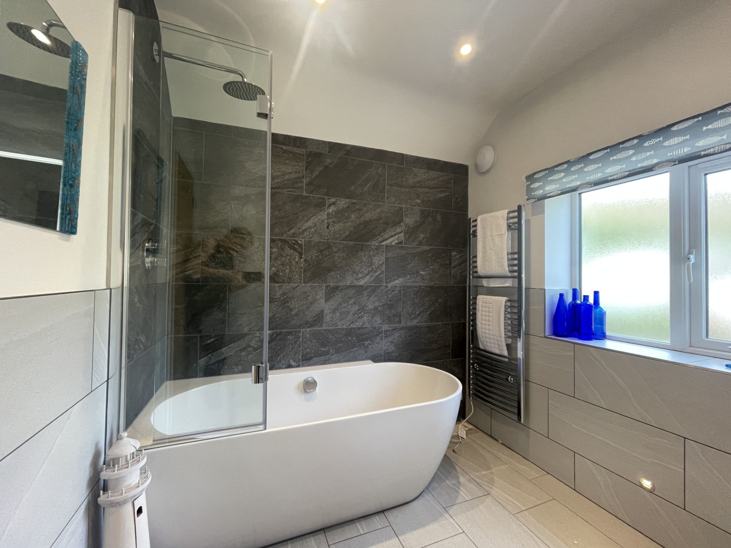A modern bathroom with large bath and overhead waterfall shower